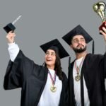 a man and woman wearing graduation gowns and holding a trophy